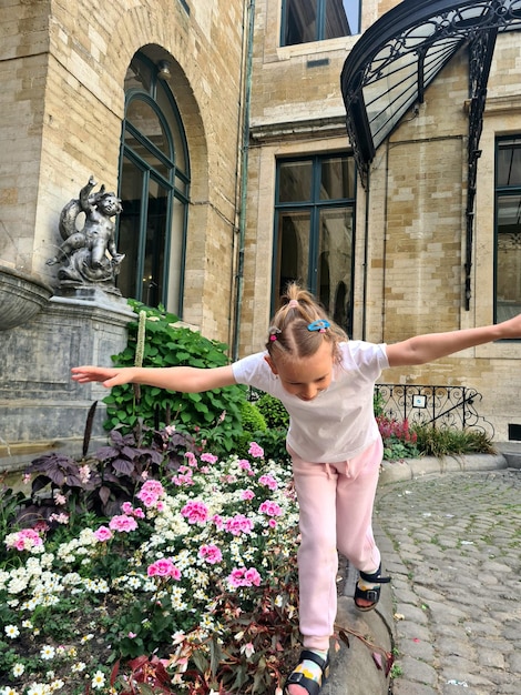 A little girl is in front of a building with a statue in the background.