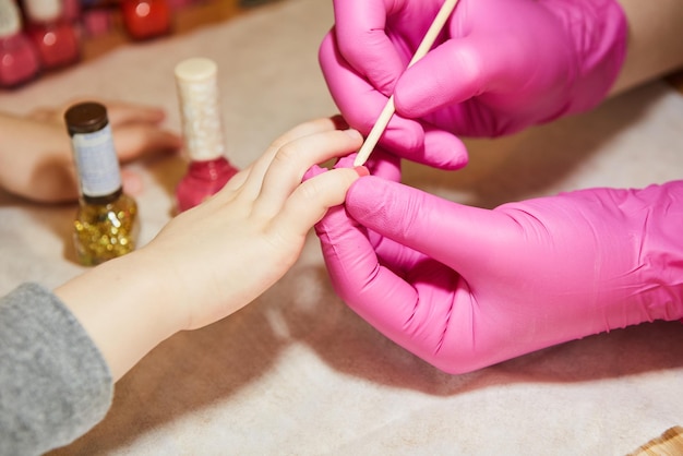 Little girl is getting manicure in beauty salon closeup