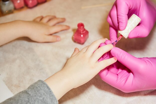 Little girl is getting manicure in beauty salon closeup