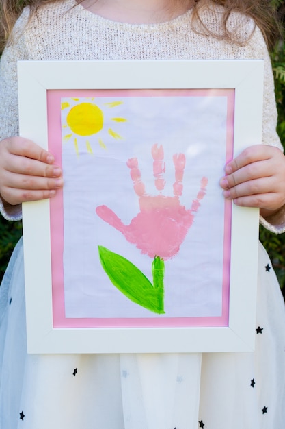 a little girl is holding a drawing in a white frame. palm flower print