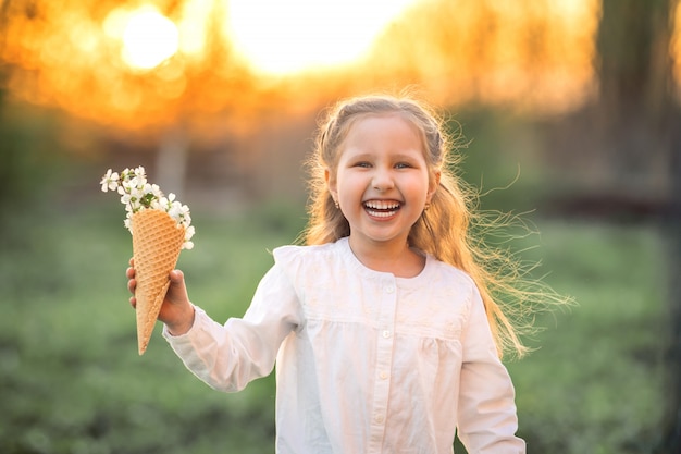 Little girl is laughing and holding tree's spring flowers in waffle cone in hand