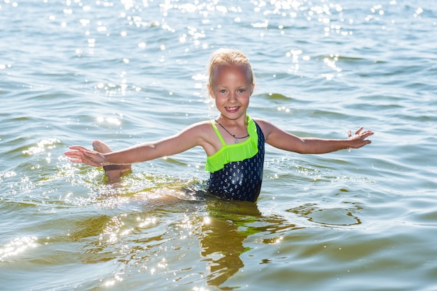 Маленькая девочка смеется и плавает в море в солнечный день