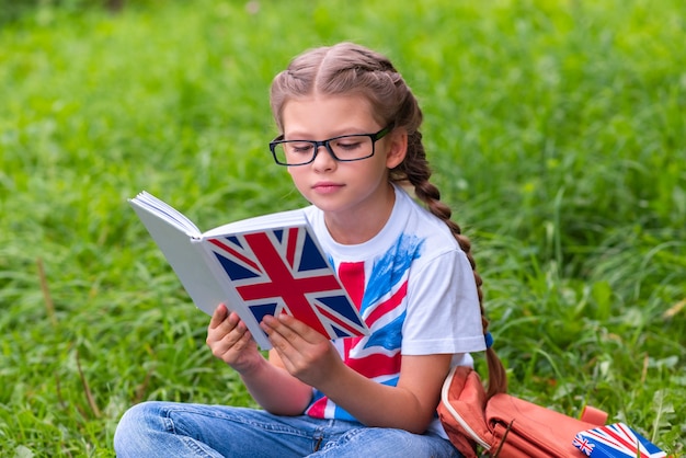 A little girl is learning English sitting on the lawn.