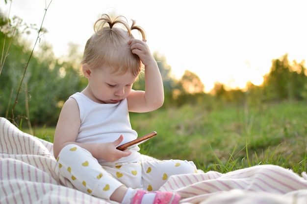 A little girl is looking at her phone she is sitting on a blanket in a field