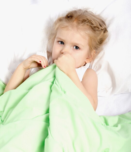 A little girl is lying in bed under a blanket. 