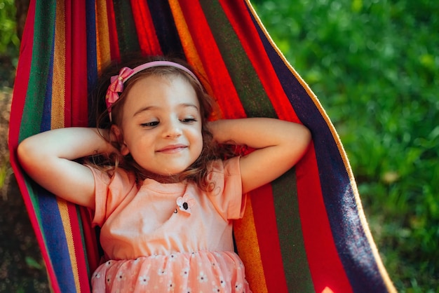小さな女の子が夏の公園のハンモックに横たわっています