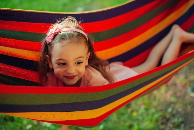 little girl is lying in a hammock in a summer park