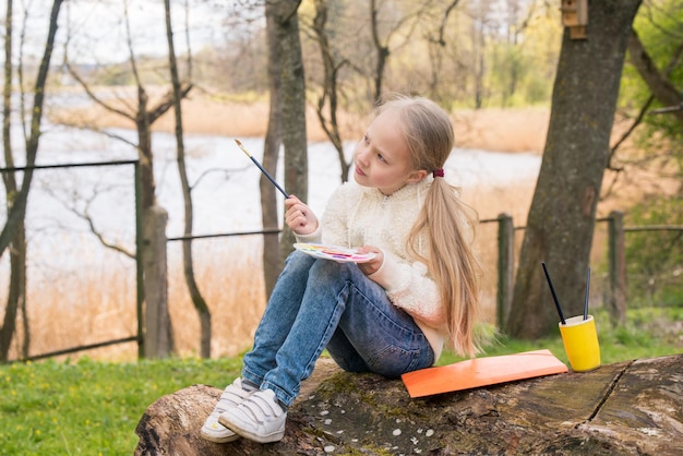 Little girl is painting picture in the spring outdoors on nature