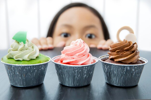 사진 어린 소녀가 맛있는 컵케이크를 엿보고 있다