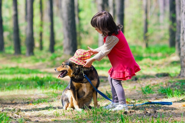 A little girl is petting a dog in the woods.