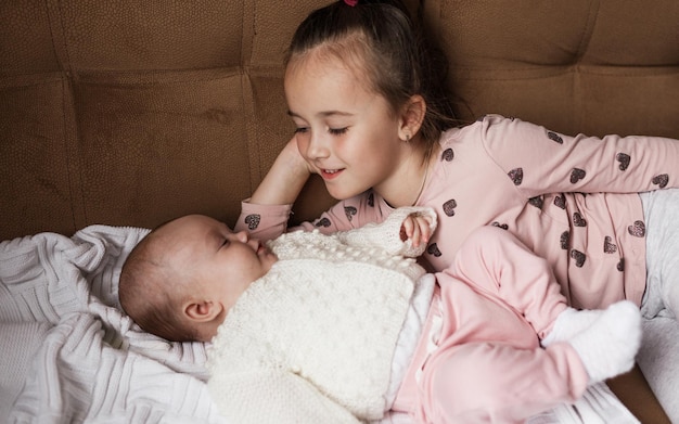 A little girl is playing on the bed with her newborn sister.