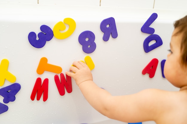 Little girl is playing foam lettern in the bath. Learning abc with play. Montessori activity