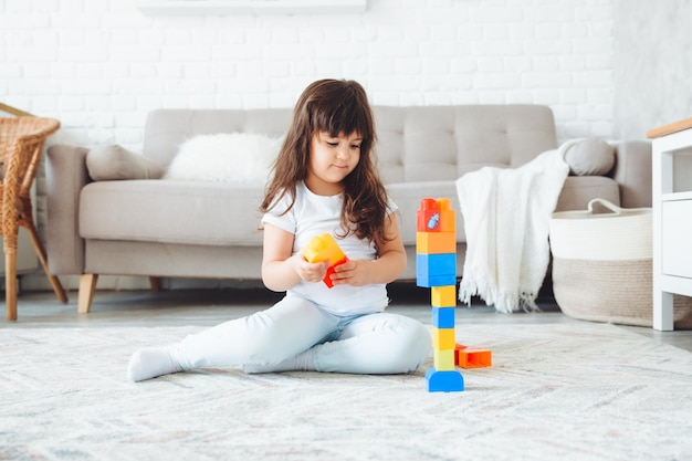 A little girl is playing with a color constructor at home on the floor