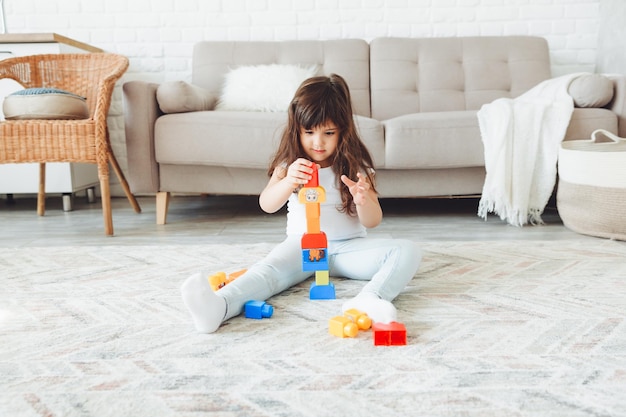 Маленькая девочка играет с цветным конструктором дома на полу