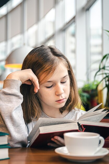 小さな女の子がお茶を飲みながらカフェに座って本を読んでいます