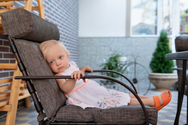 Little girl is resting in a large chair Child is sitting in chair in cafe