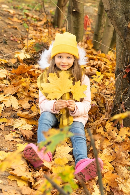 A little girl is sitting on autumn fallen leaves.