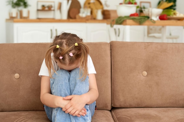 어린 소녀가 집 소파에 앉아 슬퍼하고 있습니다. 가정 폭력 및 학대 개념
