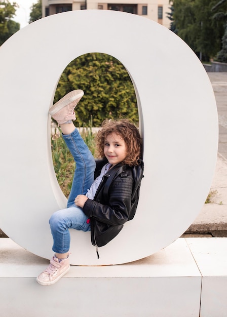 The little girl is sitting in the large letter in the city