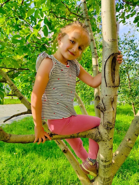 Photo a little girl is sitting on a tree branch and smiling.