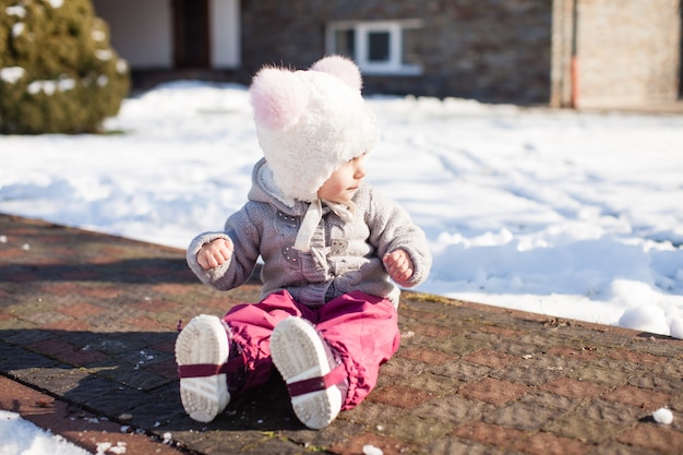 Little girl is sitting at the way in waterproof pants in cold sunny winter day