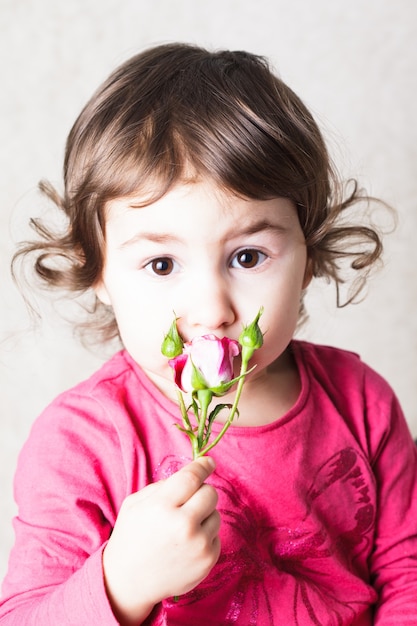 小さな女の子がバラの匂いを嗅いでいます。顔をクローズアップ
