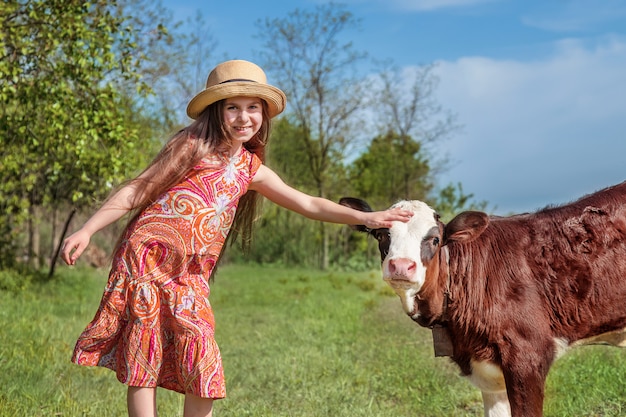 小さな女の子は、フィールドで子牛をなでます。