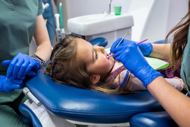 A little girl is treated for small teeth in a dental chair by a qualified pediatrician