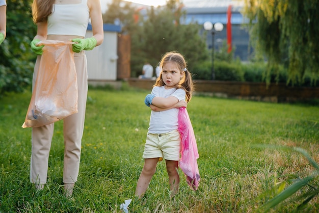 Маленькая девочка расстроена уборкой мусора в парке во время заката. Забота об окружающей среде, переработка.