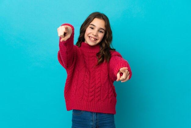 Little girl isolated on blue wall pointing front with happy expression