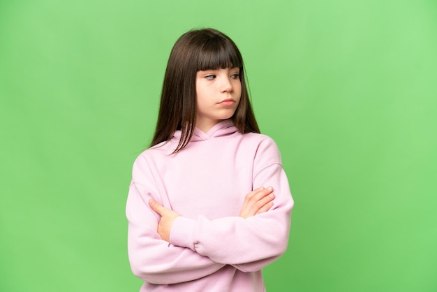Little girl over isolated green chroma key background keeping the arms crossed
