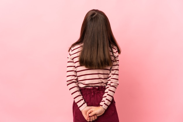 Little girl isolated on pink background in back position and looking back