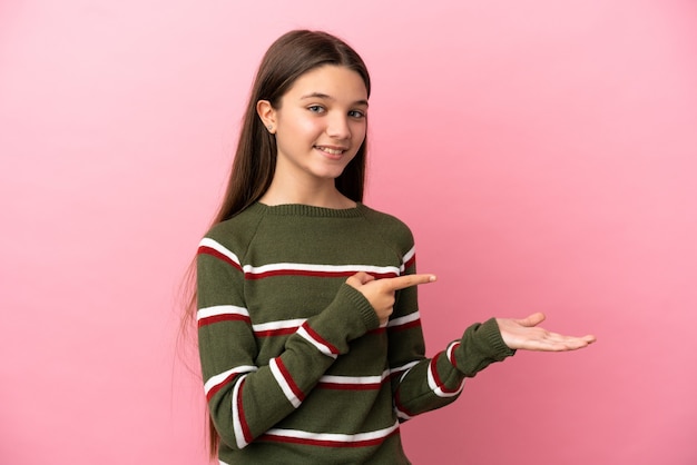 Little girl over isolated pink background holding copyspace imaginary on the palm to insert an ad