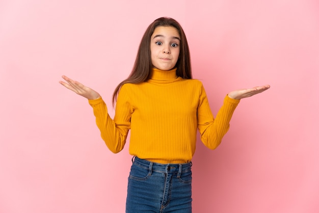 Little girl isolated on pink background making doubts gesture