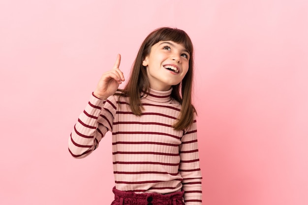 Little girl isolated on pink background pointing up and surprised