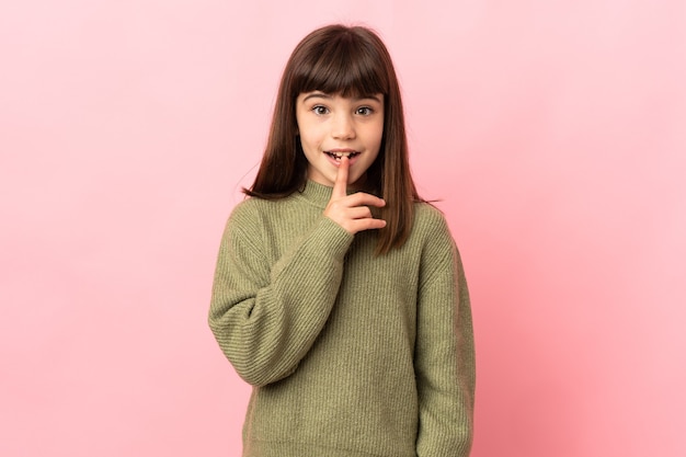 Photo little girl isolated on pink background showing a sign of silence gesture putting finger in mouth