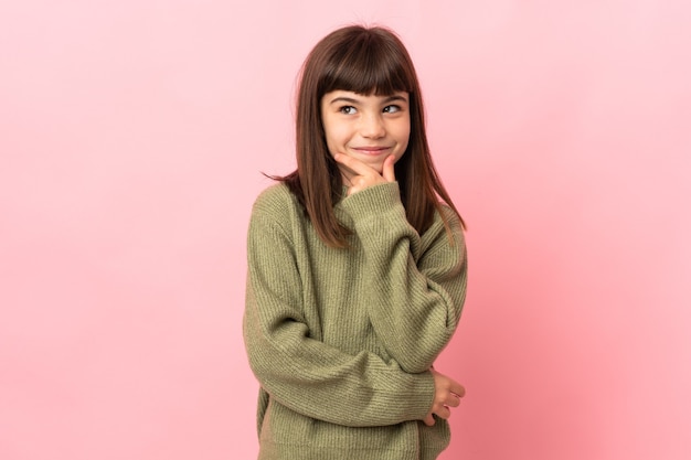 Little girl isolated on pink background thinking an idea while looking up