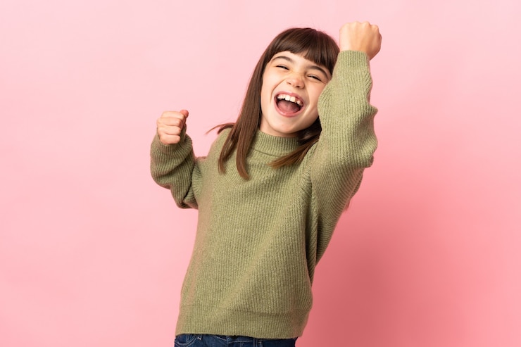 Photo 勝利を祝うピンクの壁に孤立した少女