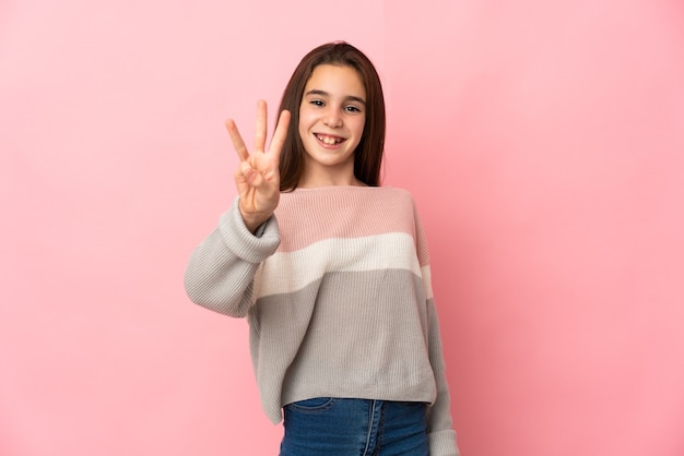 Little girl isolated on pink wall happy and counting three with fingers