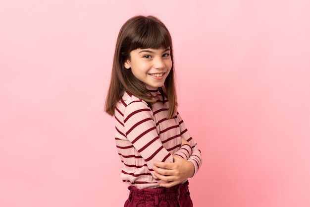 Little girl isolated on pink wall looking to the side and smiling