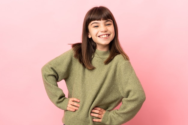 Little girl isolated on pink wall posing with arms at hip and smiling