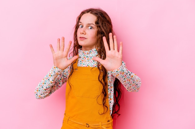 Little girl isolated on pink wall rejecting someone showing a gesture of disgust