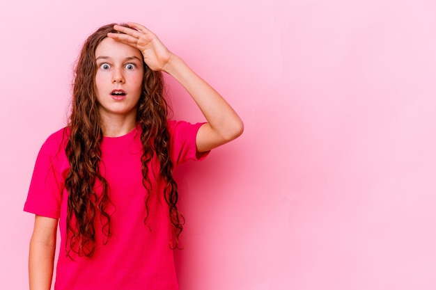 Little girl isolated on pink wall shouts loud, keeps eyes opened and hands tense