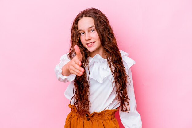 Little girl isolated on pink wall stretching hand at camera in greeting gesture