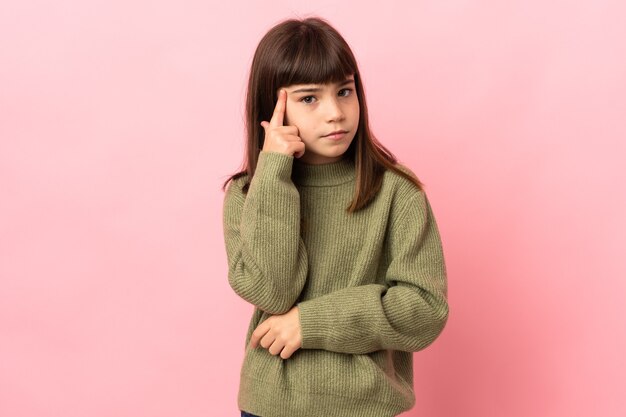 Little girl isolated on pink wall thinking an idea