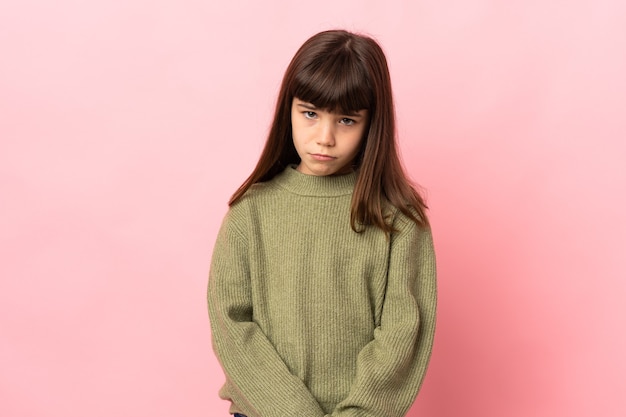 Little girl isolated on pink wall with sad expression