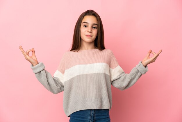 Little girl isolated on pink wall in zen pose