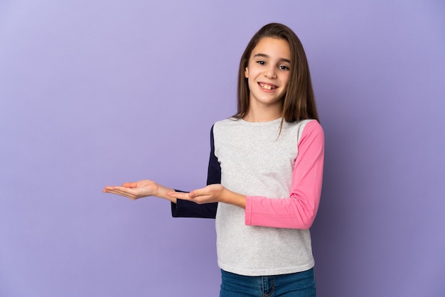 Little girl isolated on purple wall extending hands to the side for inviting to come