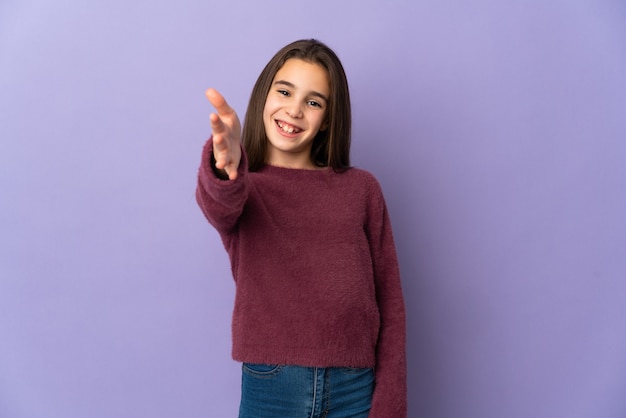 Little girl isolated on purple wall shaking hands for closing a good deal