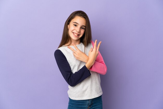 Little girl isolated on purple wall smiling and showing victory sign